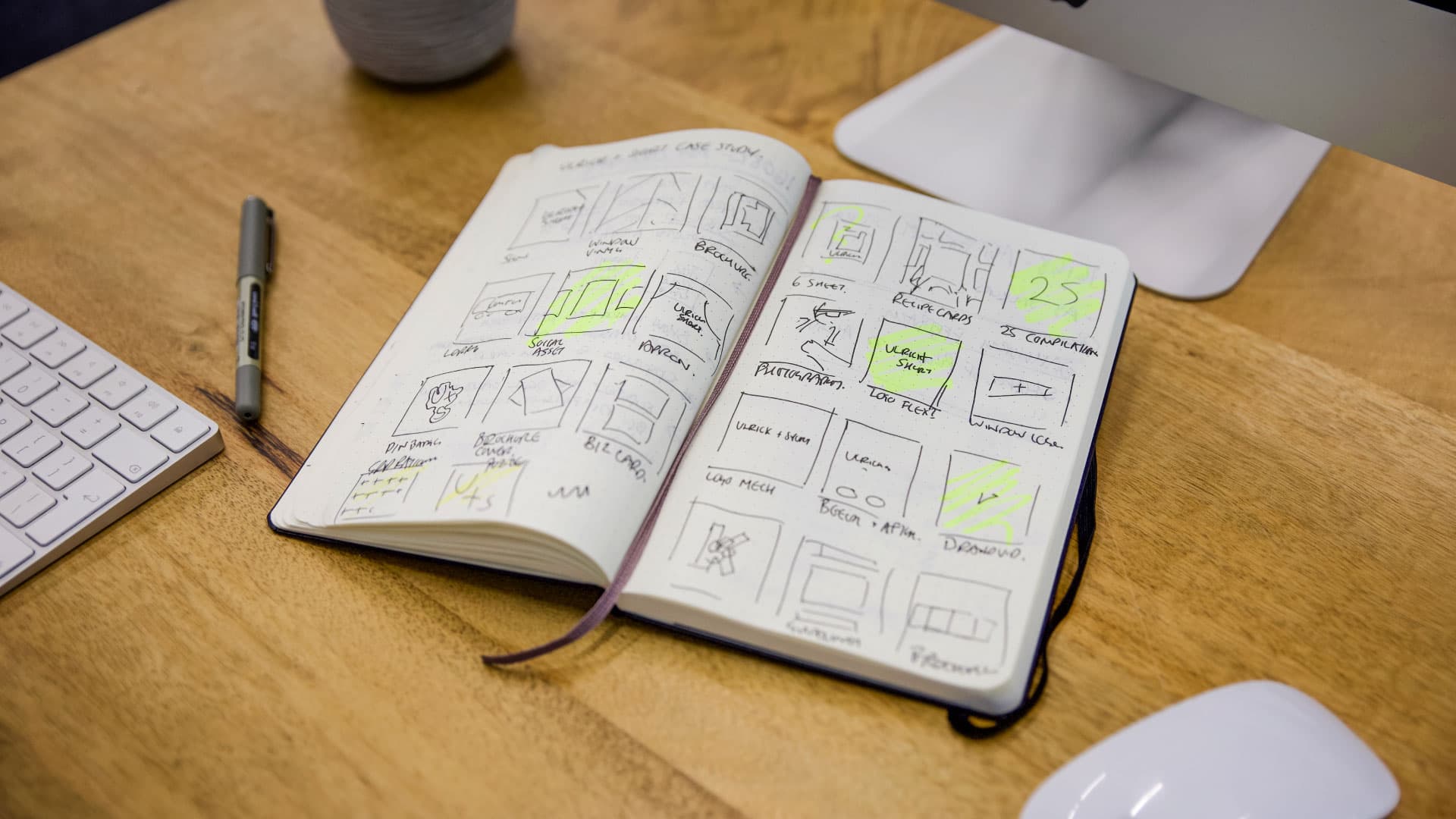 Sổ tay Moleskine mở trên bàn gỗ, hiển thị các bản phác thảo thiết kế cùng bảng màu vàng nổi bật.