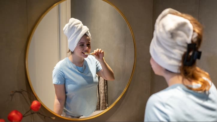 Một phụ nữ quấn khăn trắng trên đầu đánh răng trước gương sau khi tắm trước khi đi ngủ