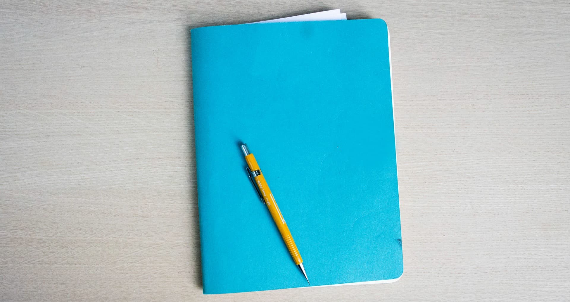 Sổ Moleskine Cahier XL màu ngọc lam với bút chì kim màu vàng đặt chéo trên bìa.