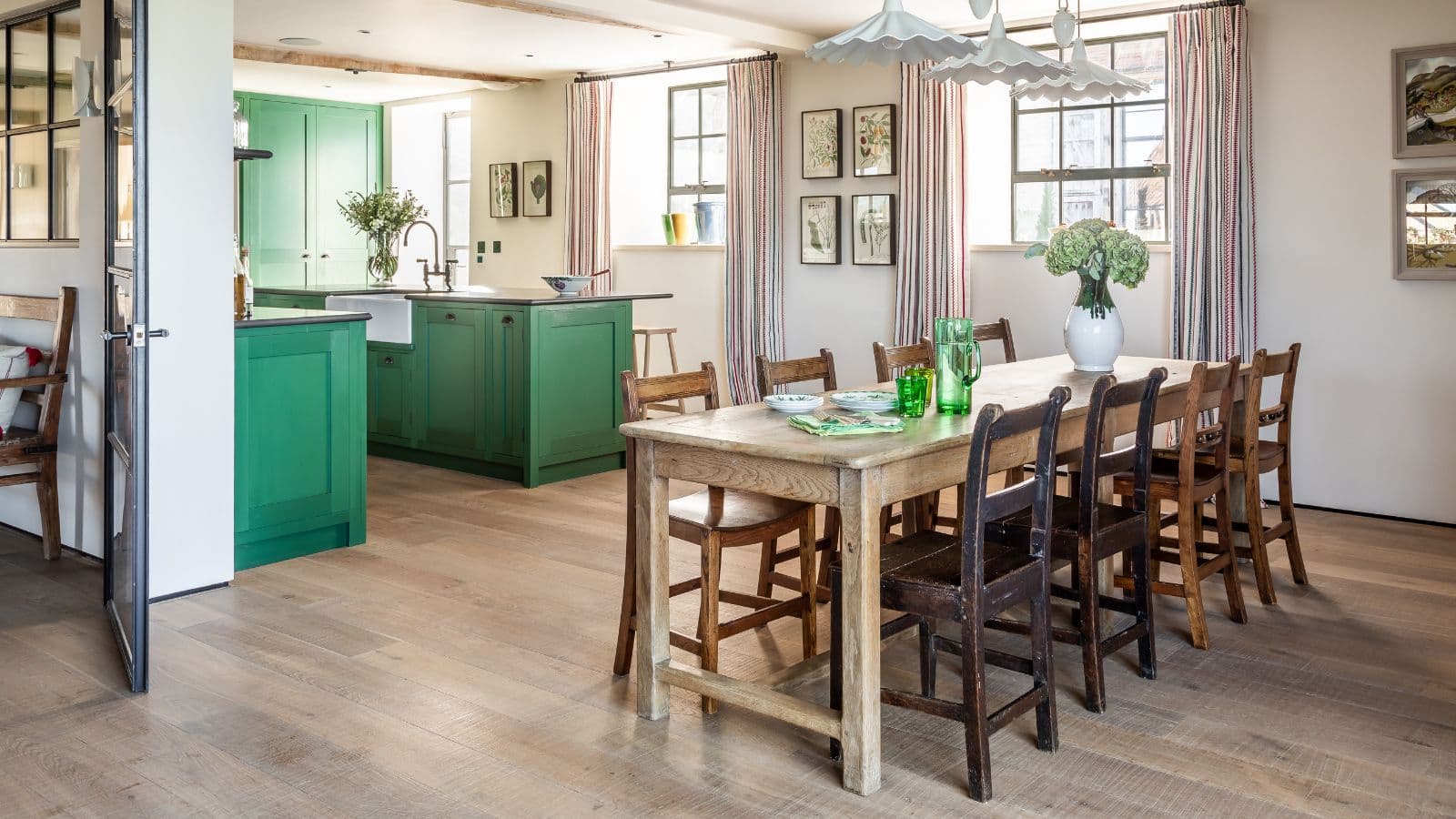 Một nhà bếp phong cách country với tủ bếp xanh lục ở nền và bàn ăn gỗ sáu ghế phía trước.