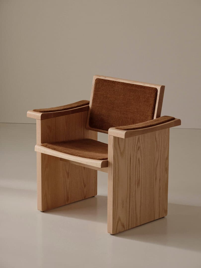 A wooden armchair with a minimalist design, featuring a rectangular frame and flat armrests, with brown cushioned seat, back, and arm pads.