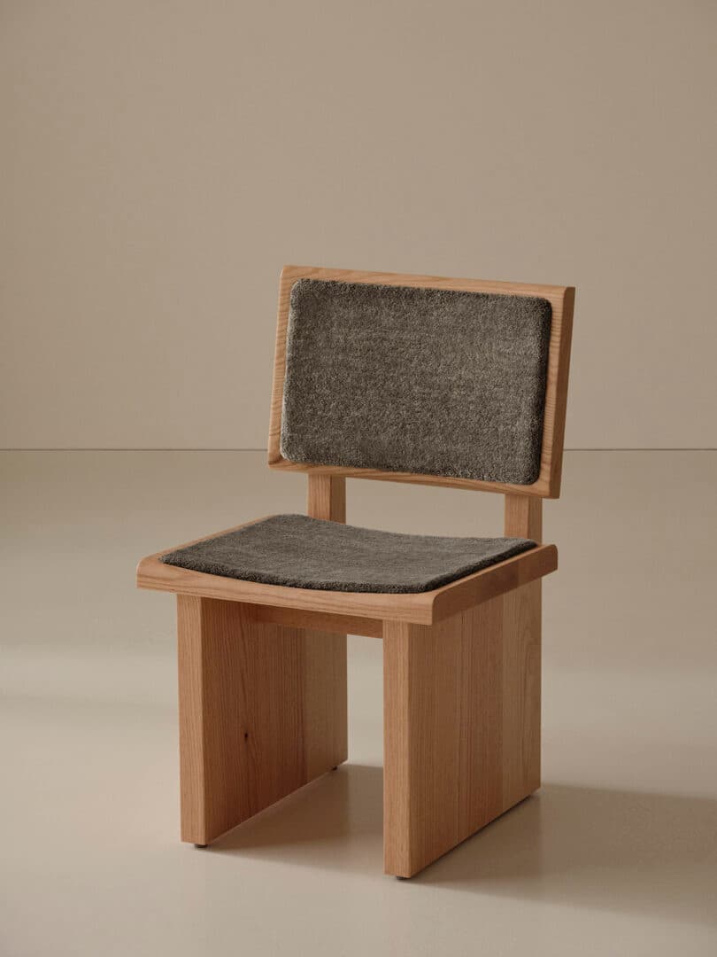 A wooden chair with a minimalist design, featuring a rectangular backrest and seat, both cushioned with gray fabric upholstery.