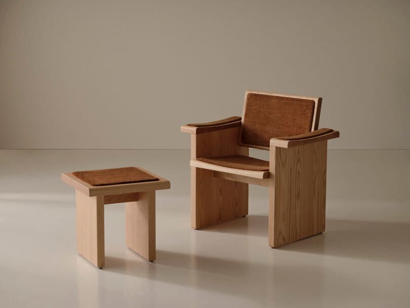 A wooden chair with a brown seat and backrest pad is positioned next to a matching wooden stool in a minimalist room with a neutral background.