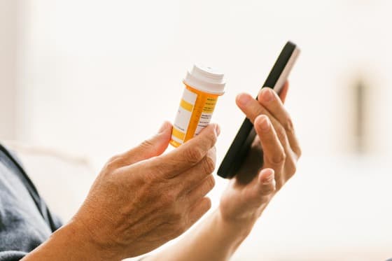 Holding his medication, the man listens to doctor on phone