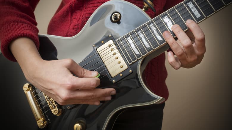 Cận cảnh một phụ nữ chơi cây Les Paul màu xám slate với pick màu xanh.