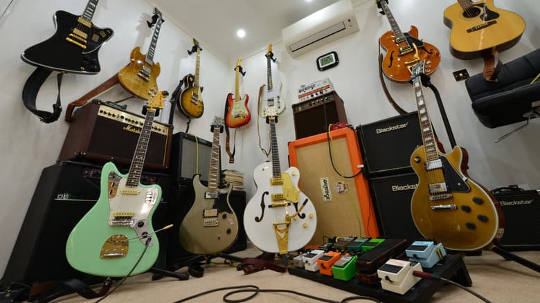Một số cây guitar, bao gồm các mẫu Gibson (các loại hollow body và Les Paul), cùng với dãy ampli và bảng pedal.